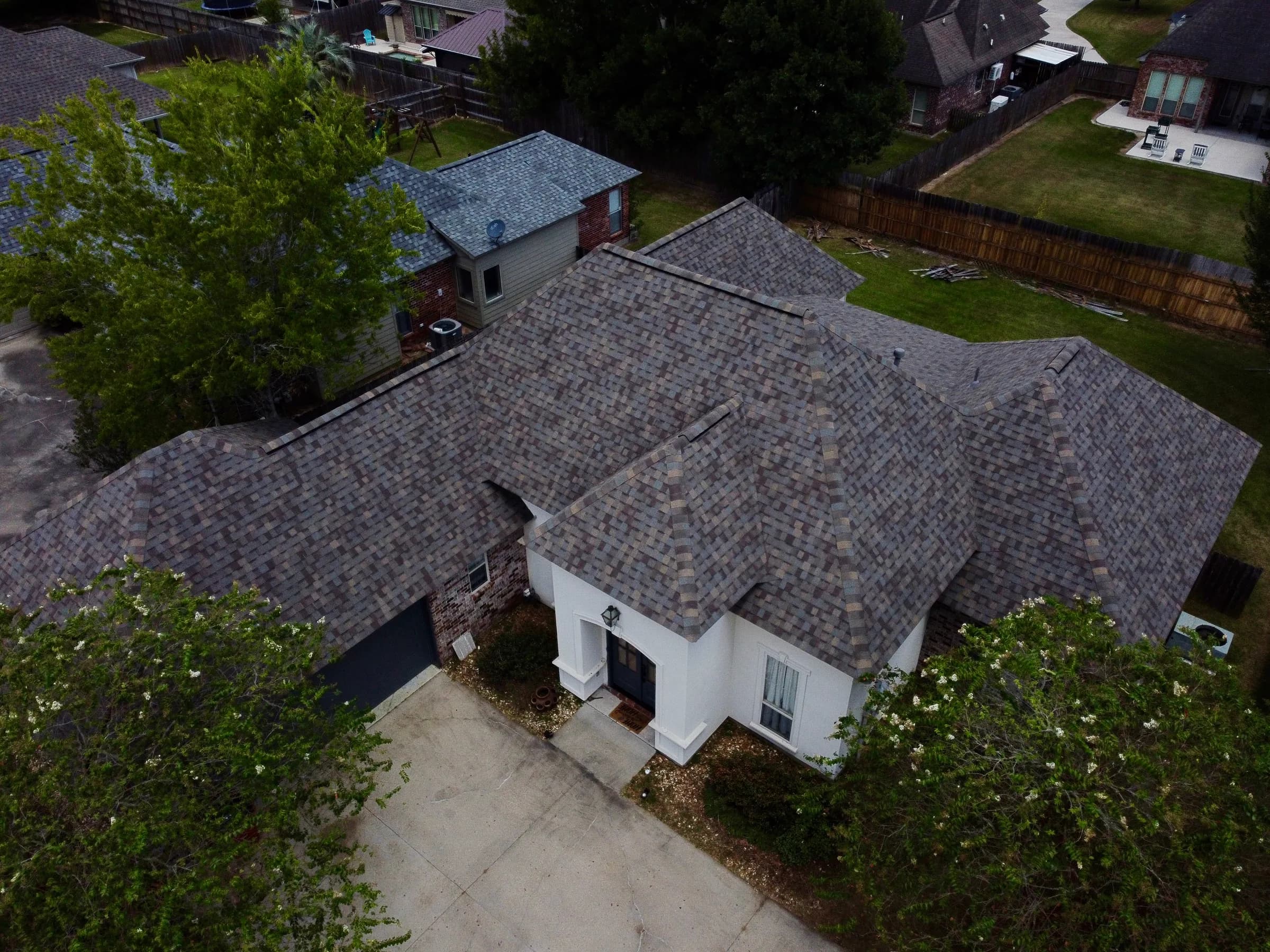 Drone view of a finished architectural shingle roof on a white brick home
